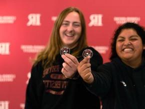 In front of red backdrop with LR logo visible, two female students hold out Bears Say Thanks stickers to foreground 